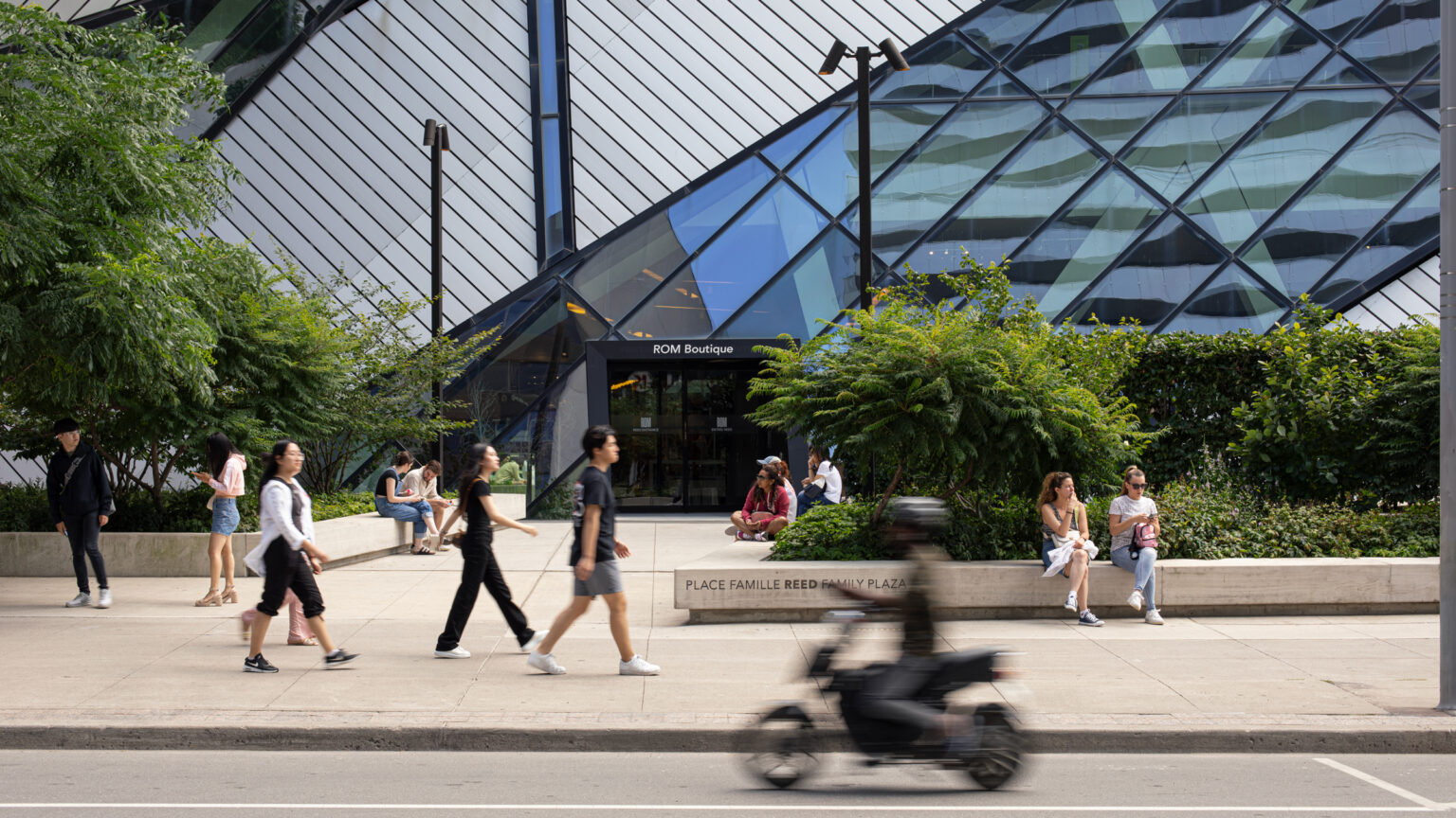 Street view of many people walking and sitting in front of the Royal Ontario Museum on Bloor Street West in Toronto, located directly across the street from Resident's Yorkville development